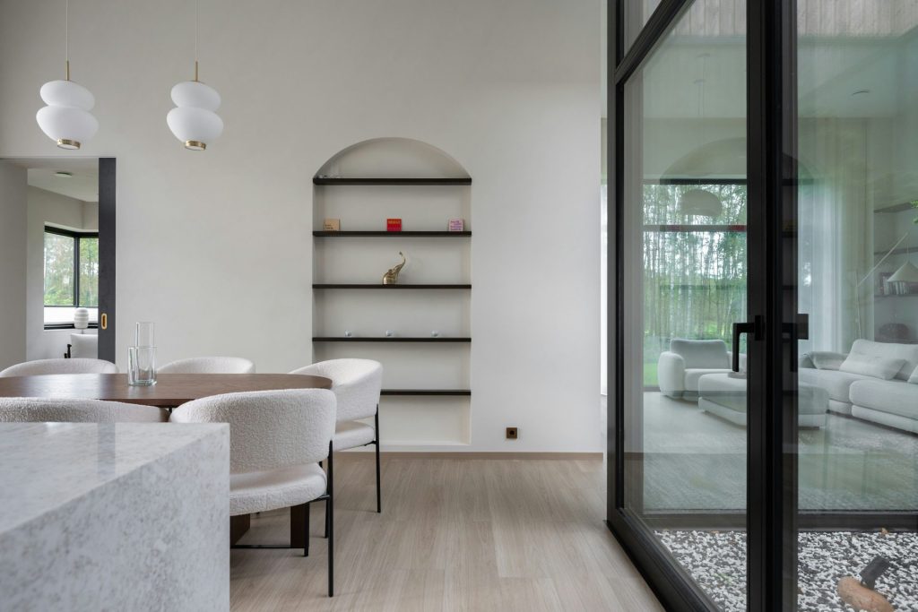 Comedor moderno con estantes arqueados y grandes ventanales.